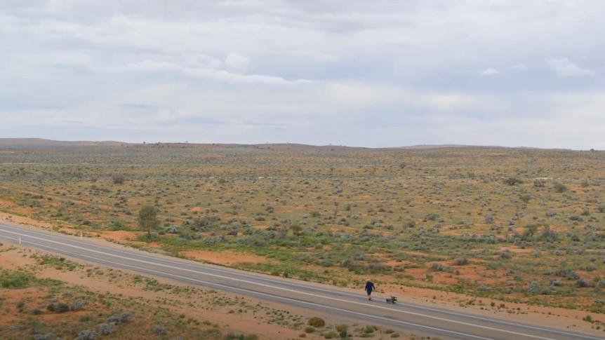 A man walking with a cart along a road in the desert near Broken Hill. 