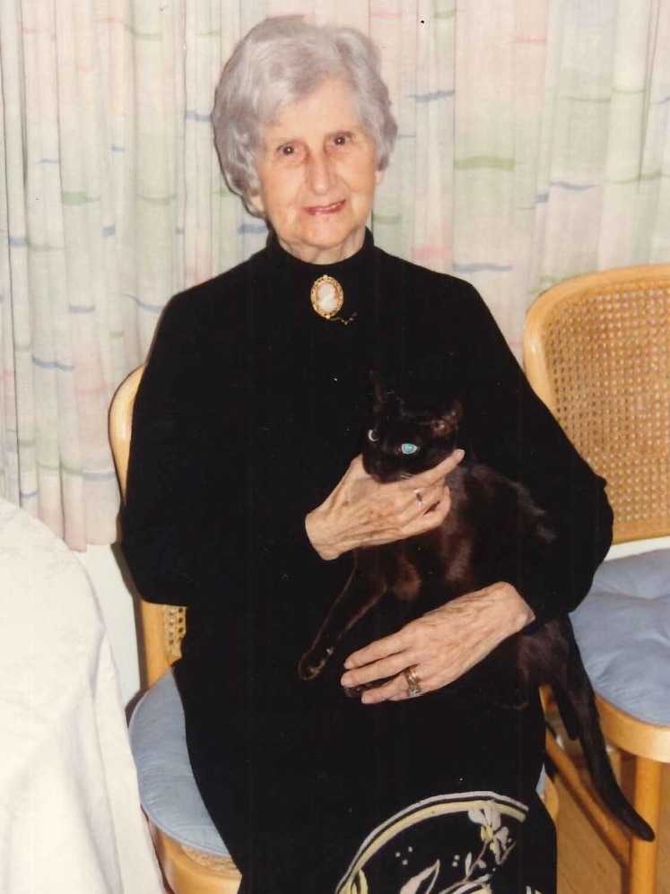 An older woman smiles as she holds a black cat.
