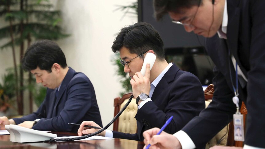An official from South Korea talks on the phone with North Korea. He has a pen and paper.