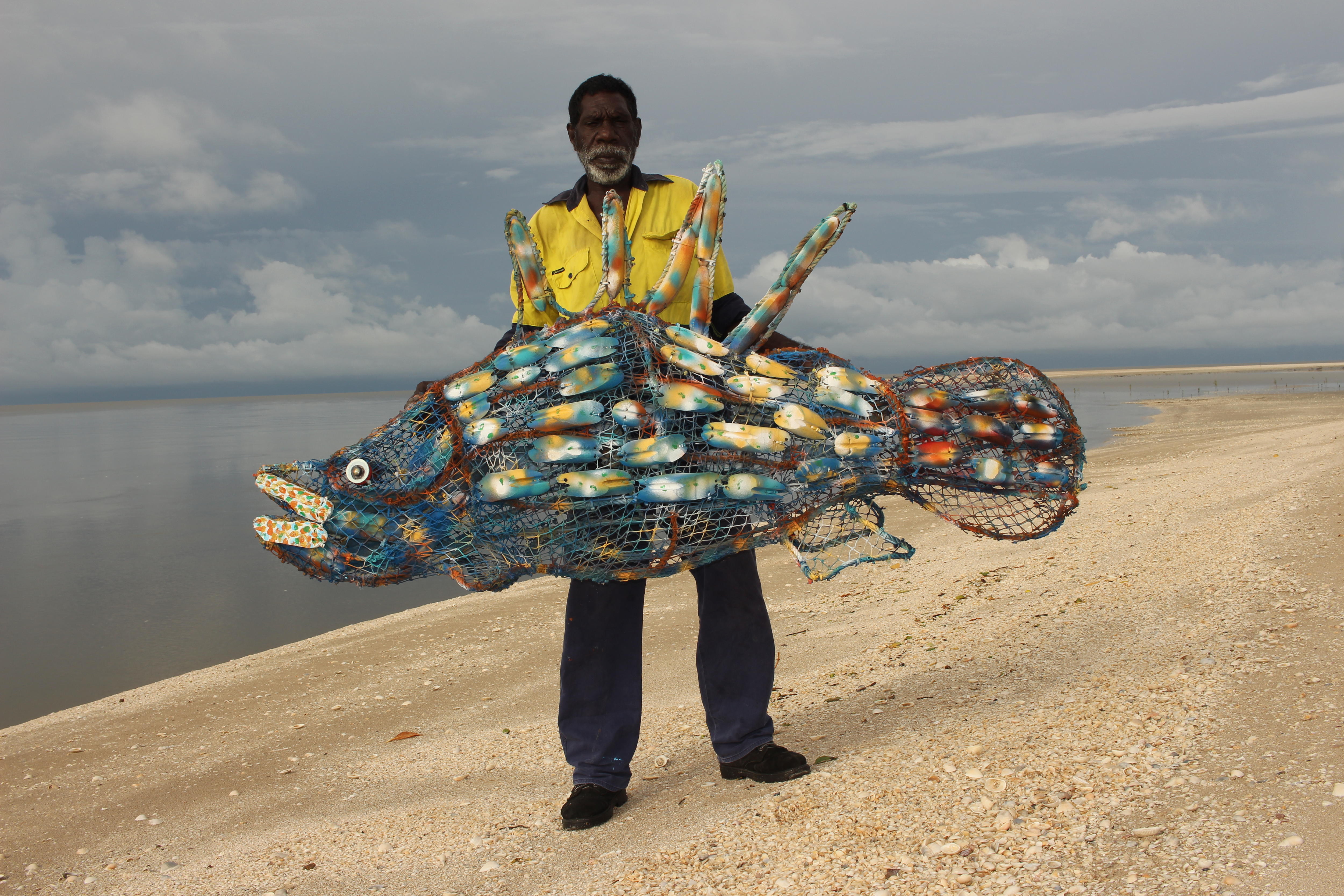 A First Nations man holds a large fish sculpture made from netting.