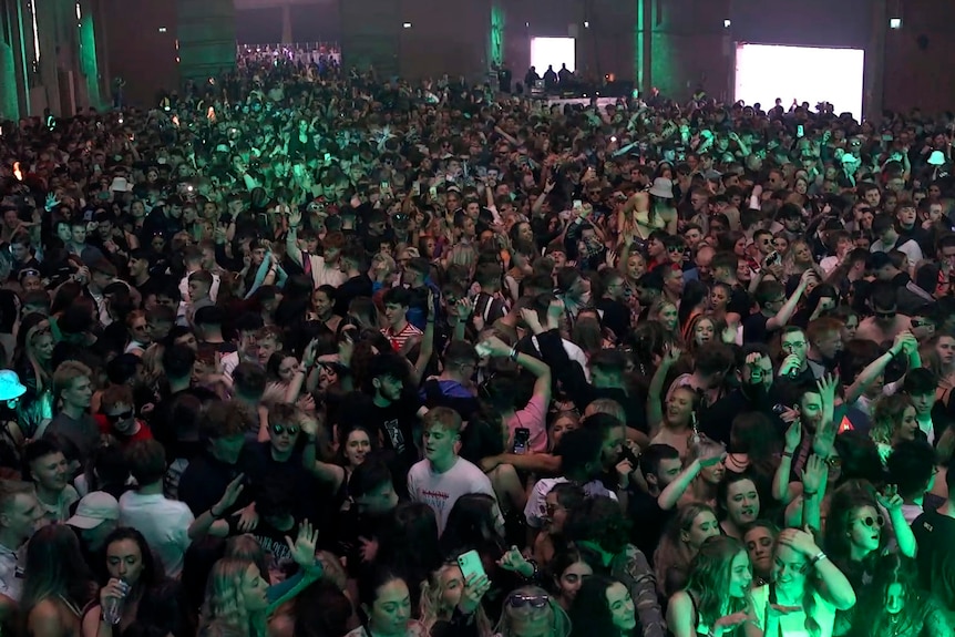 Members of a large indoor crowd dance while packed in closely without face masks.