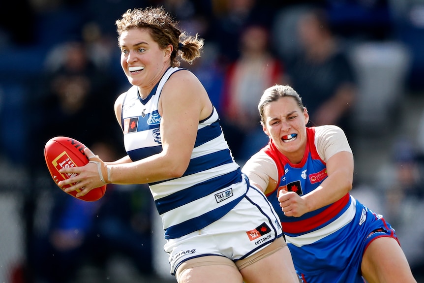 A Geelong AFLW player holds the ball while being tackled by a Western Bulldogs opponent.