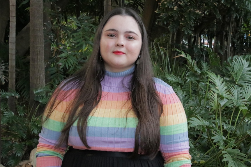 a woman with long brown hair wearing a rainbow top.