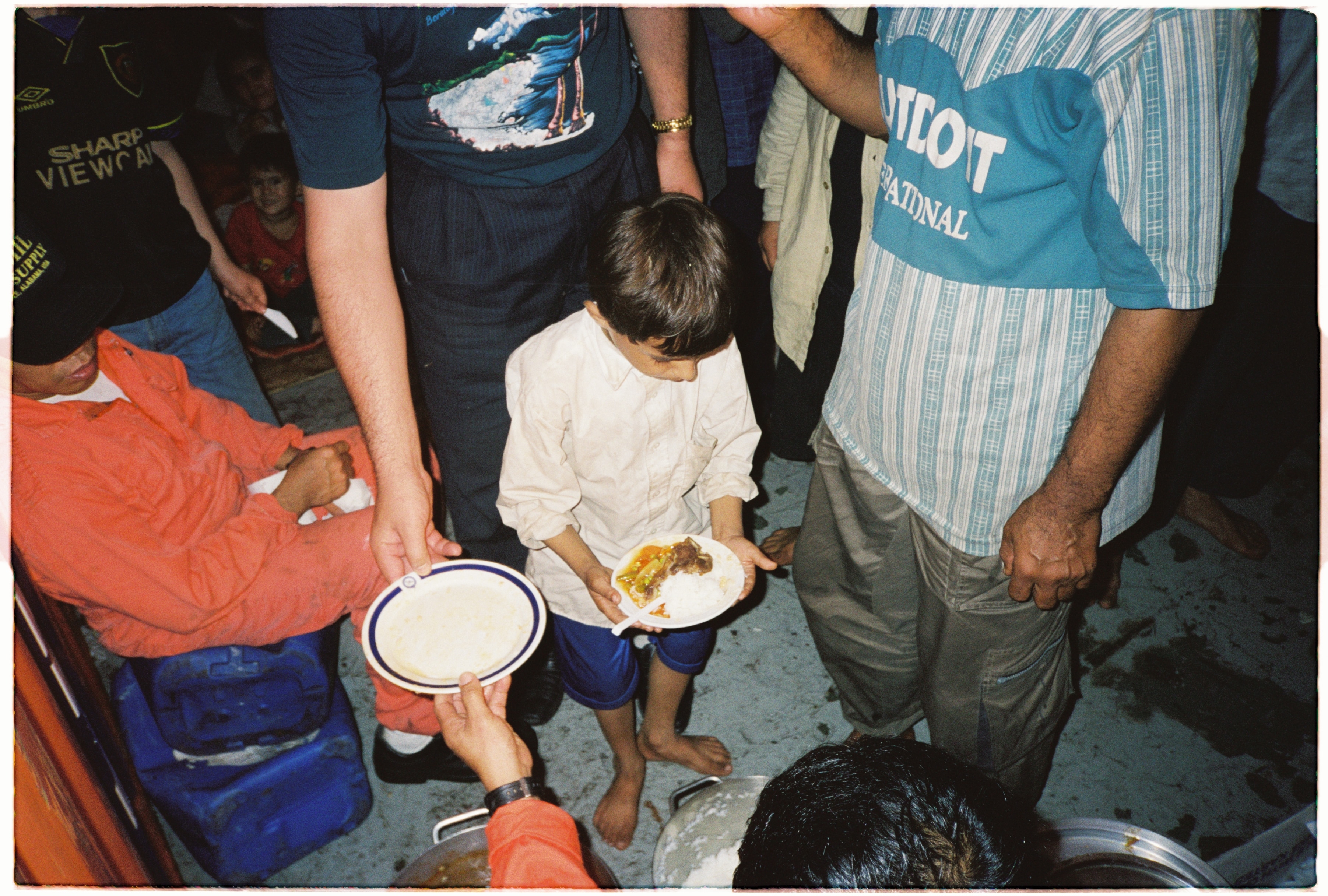A young boy holds a plate of food, surrounded by adults.