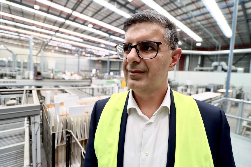 A man wearing glasses and a yellow high-vis vest stands in a factory.