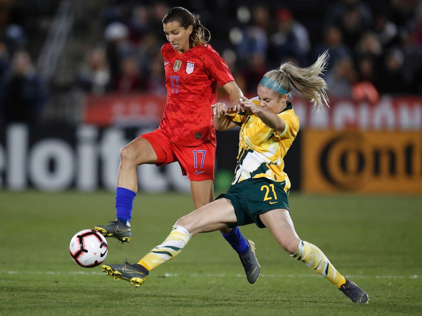 Ellie Carpenter (in yellow) slides towards Tobin Heath (wearing red) to win the ball