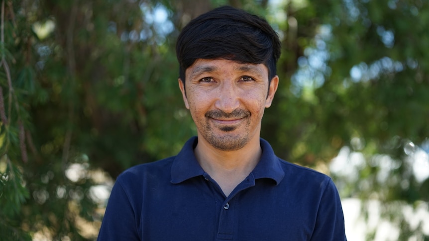 Ali Rahmani pictured smiling in front of trees wearing a navy collared shirt