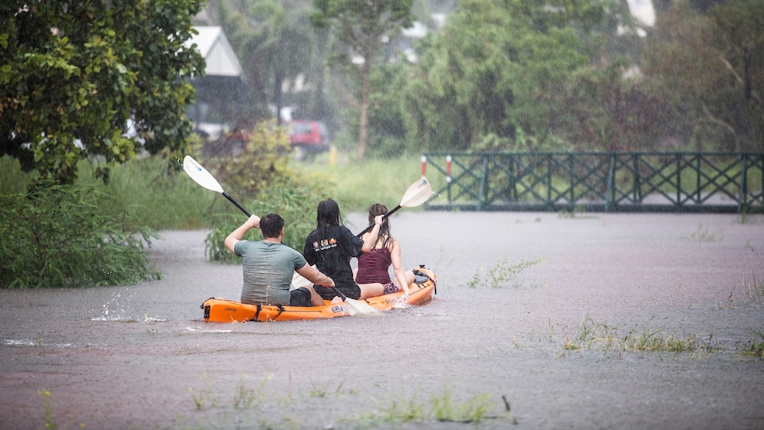 Three people in a canoe on floodwaters in Broome