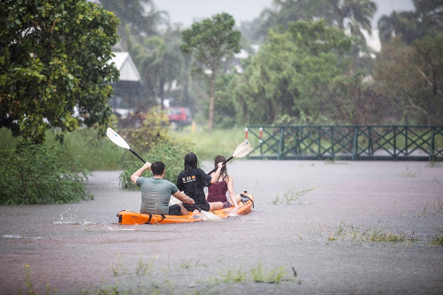 Three people in a canoe on floodwaters in Broome