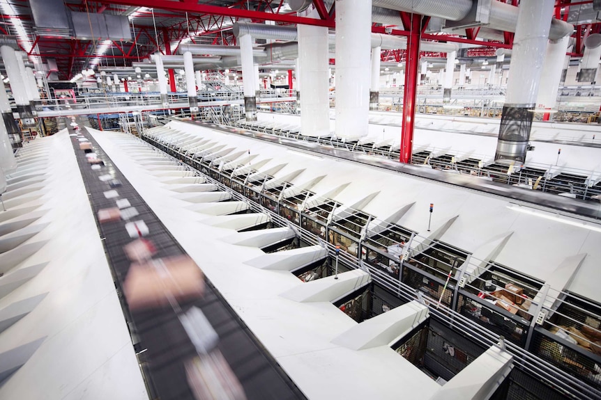 Parcels flying by on a conveyor belt inside a large red and white postal facility.