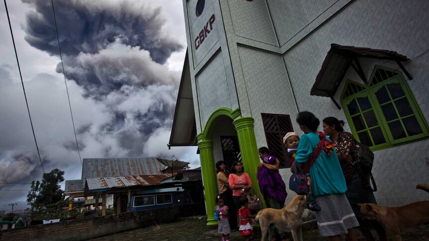 Villagers stand outside a church in Simpang Empat on November 24, 2013 following another eruption of Mount Sinabung.