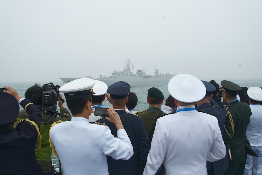 Naval officers take photos of a ship which can be seen at a foggy distance
