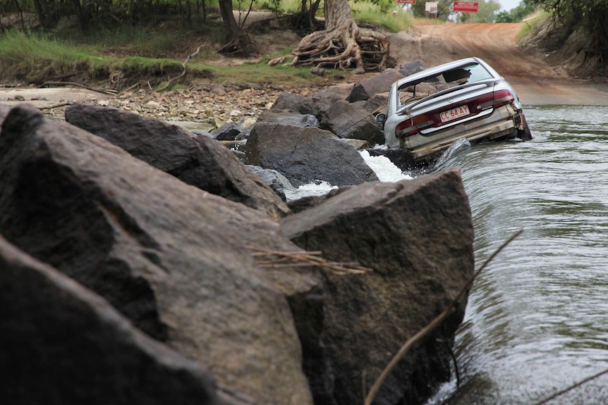 A photo of water flowing over Cahill's Crossing and a smashed up Commodore that didn't make it across.