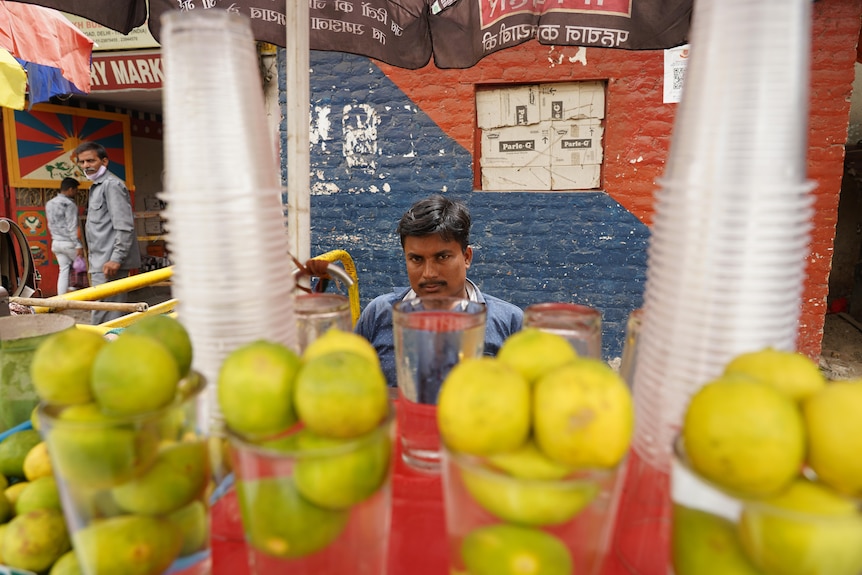 A man sits behind a mobile drinks van with water cups and limes stacked in front