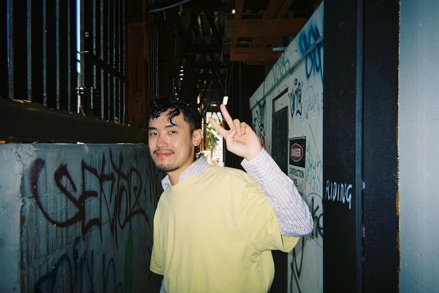 an asian man holding his hands in a graffiti alleyway