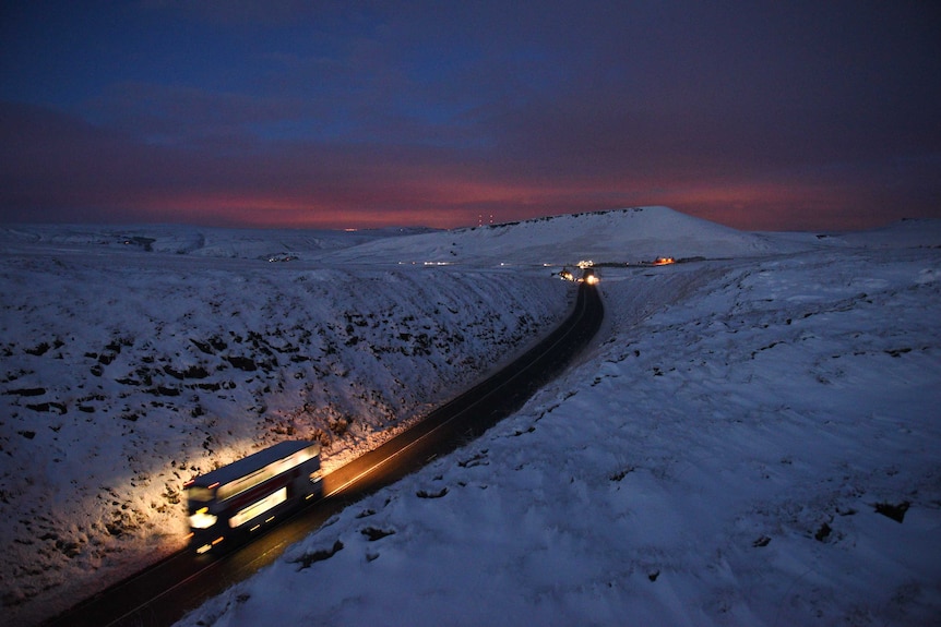 A double-decker bus travels between snow-covered fields at dusk near the village of Diggle, northern England, on December 27, 2014