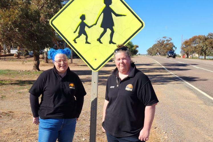Two women standing in front of a child crossing sign.