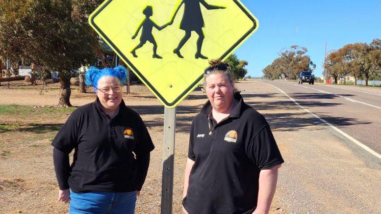 Two women standing in front of a children crossing sign.
