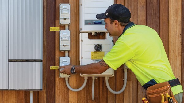 A tradesman in bright yellow working on a power meter.