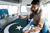 Picture of a man sitting in a car with a coffin covered with Pakistan flag