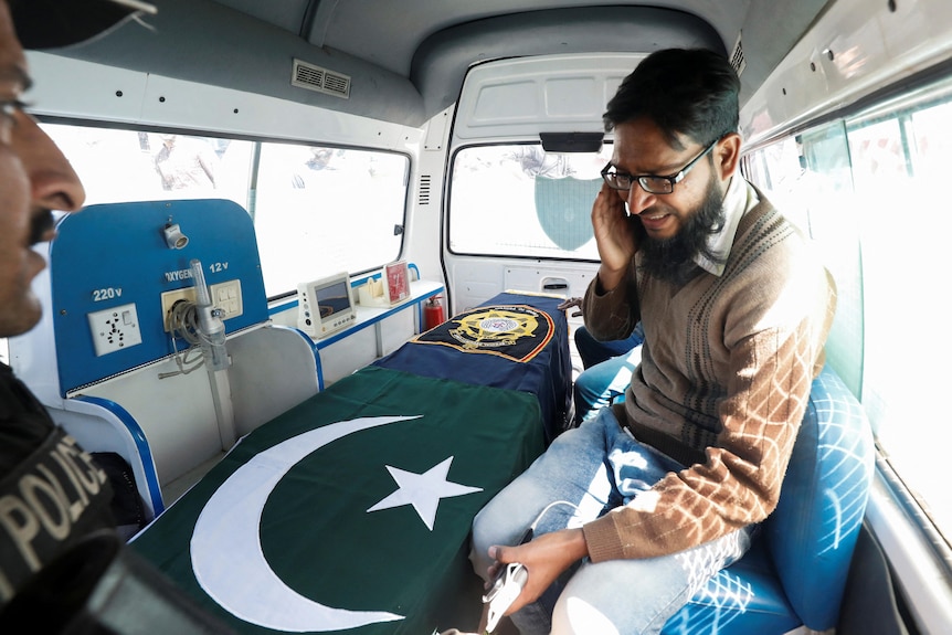 Picture of a man sitting in a car with a coffin covered with Pakistan flag