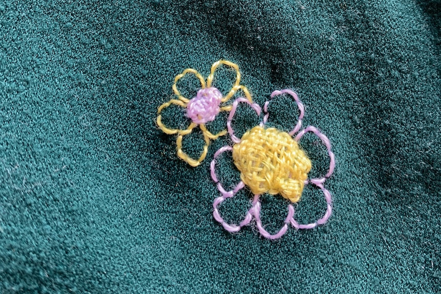 Green jumper with two small purple and yellow flowers stitched on