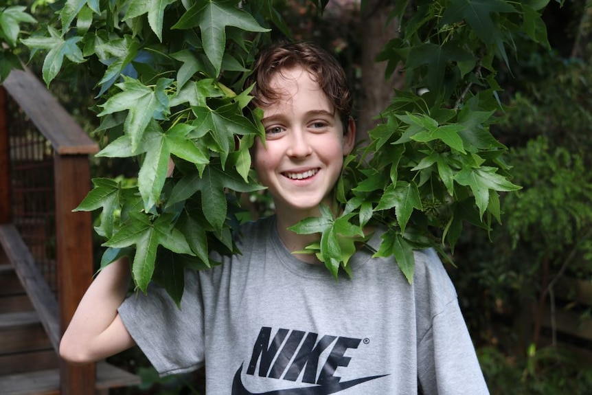 A young boy smiles next to some leaves