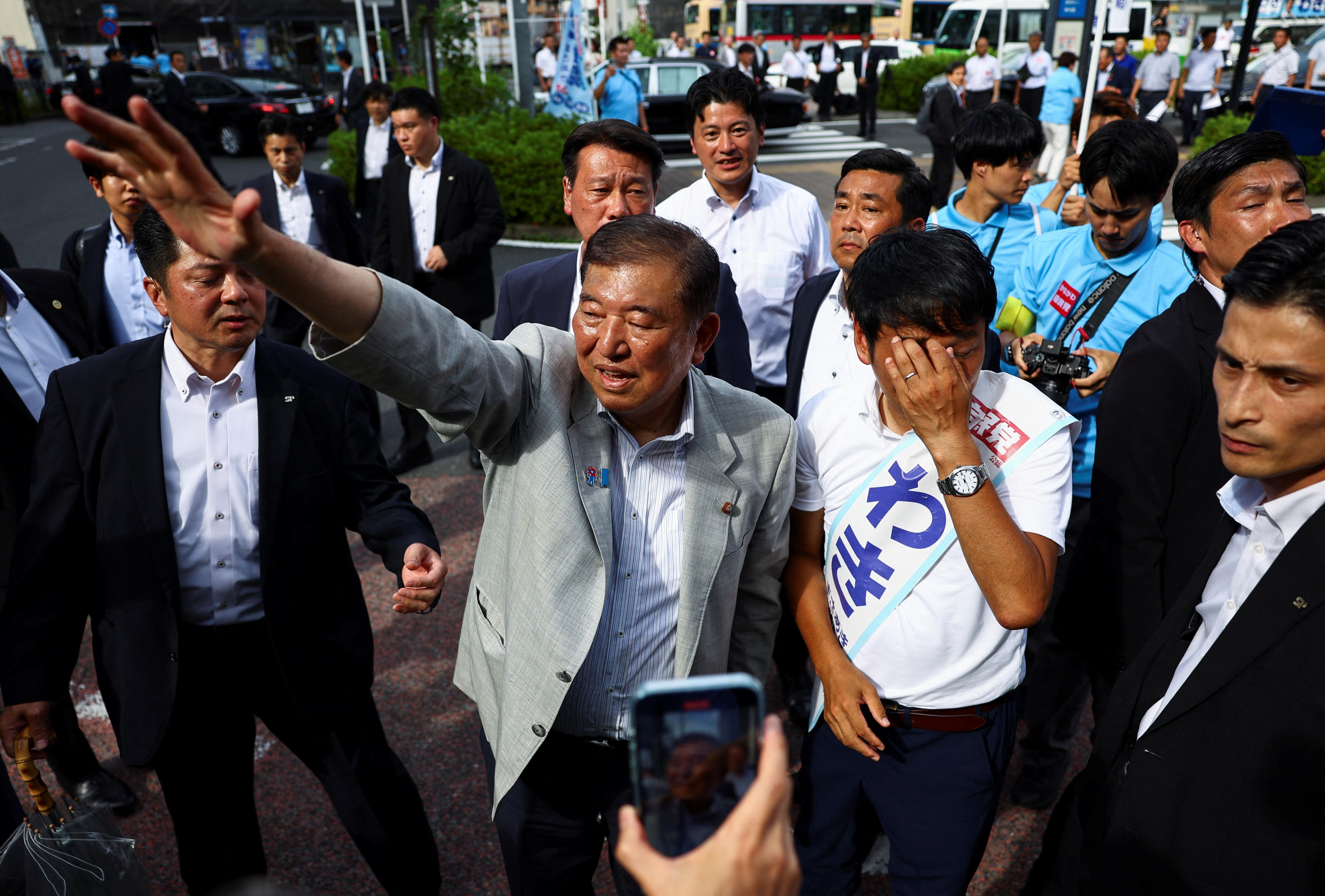 The Japanese prime minister, in a suit, waving at crowds outside a polling station.