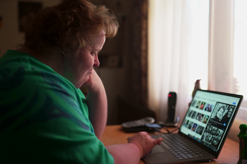 A woman with Down syndrome sitting looking at a laptop with pictures on it