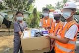 A group of people in masks and high vis vest carrying a box of medical supplies 