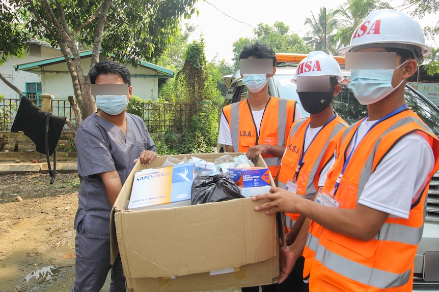 A group of people in masks and high vis vest carrying a box of medical supplies 