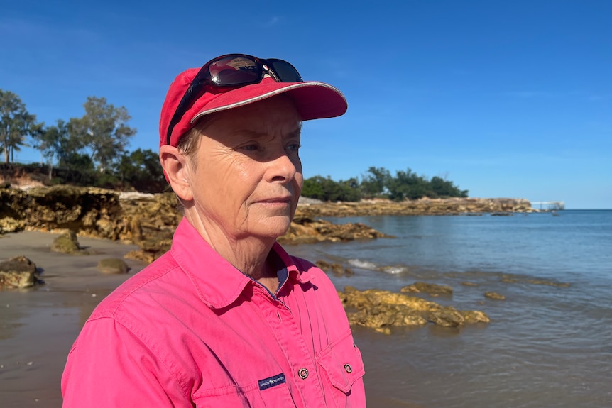 a woman wearing a pink collared shirt and red cap at the beach