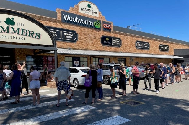 A supermarket with a large queue of people outside.