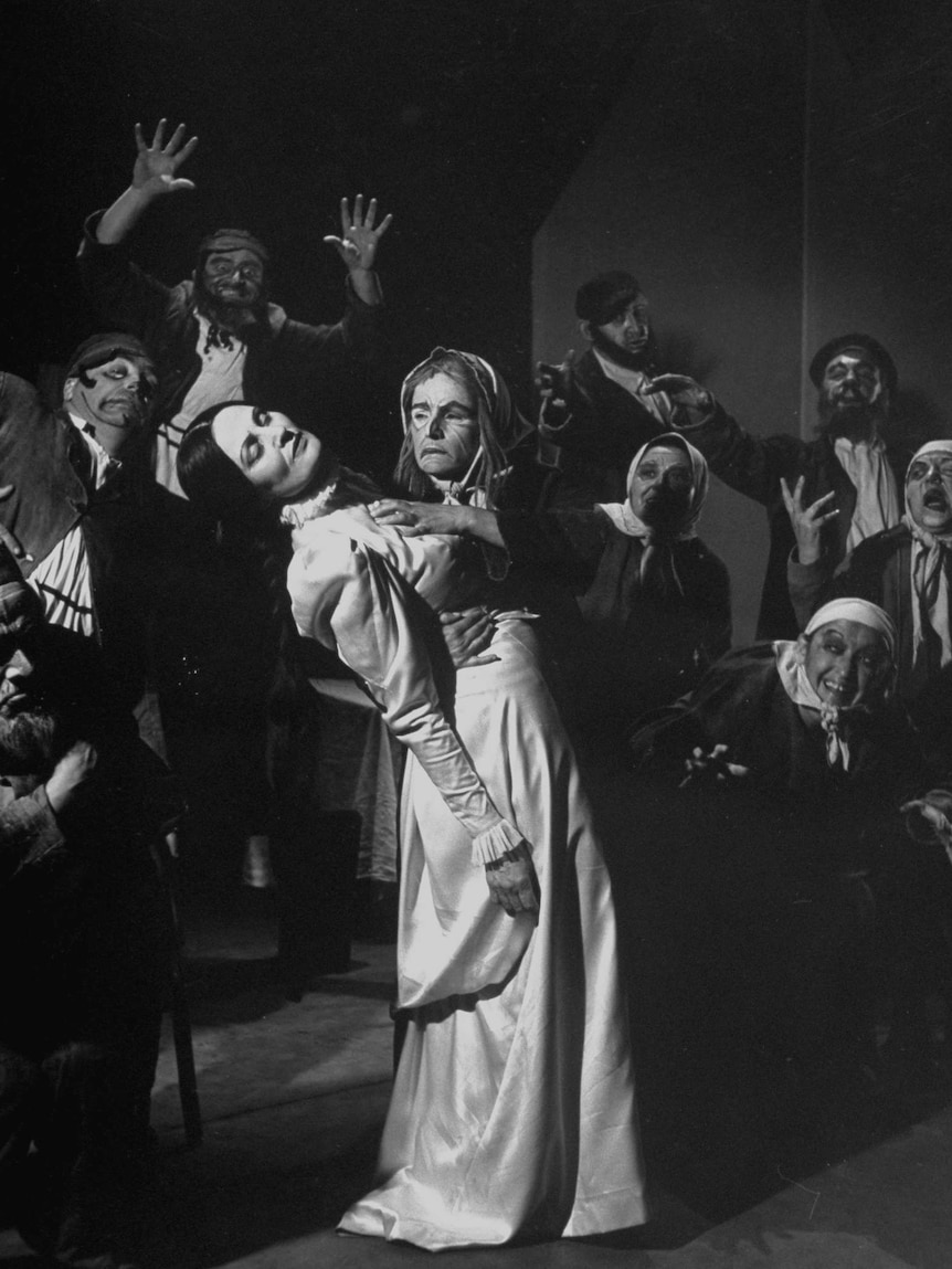 A black and white image of a 1930s play, a young bride faints in the arms of an old crone