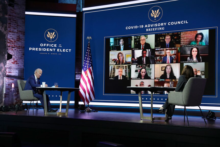 Joe Biden and Kamala Harris sit at desks as they receive a briefing via a video call.