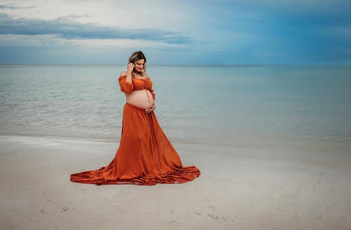 a woman in a beautiful orange dress looks at her pregnant belly.