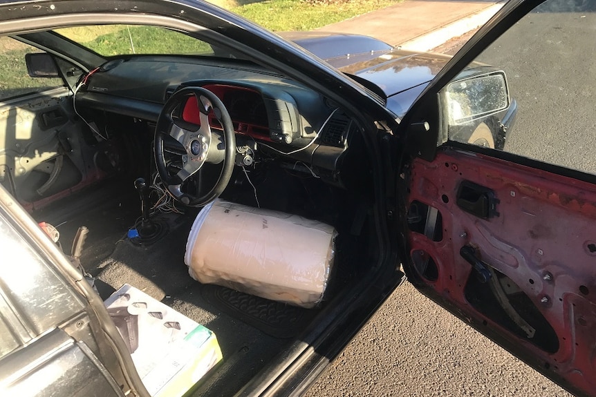 A car with its door open showing mattress to be the driver's seat.