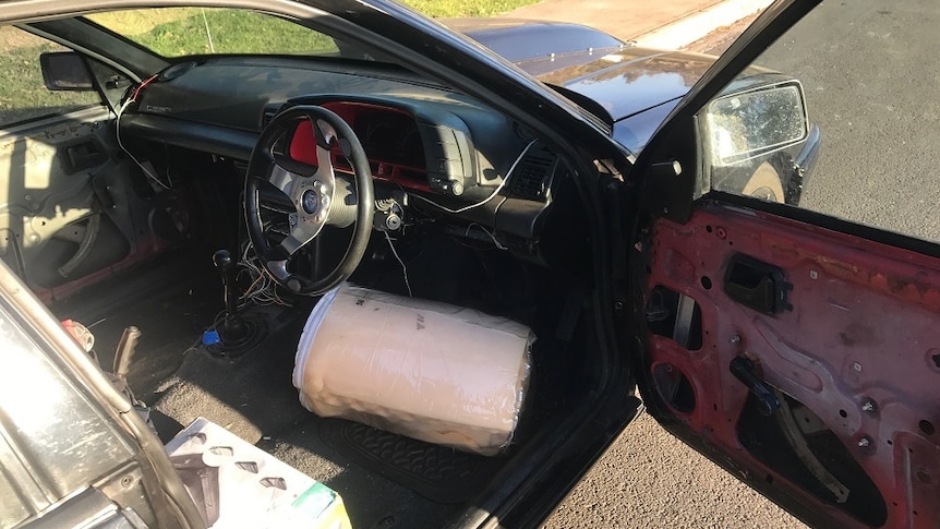 A car with its door open showing mattress to be the driver's seat.