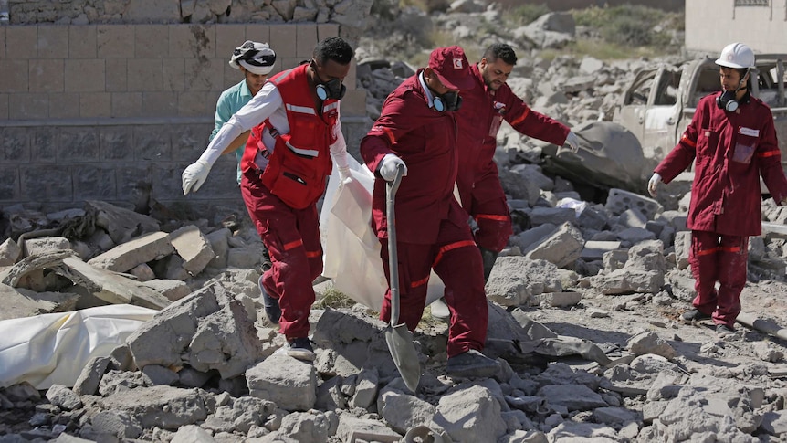 Rescue workers carry a body from under the rubble of destroyed building in Yemen