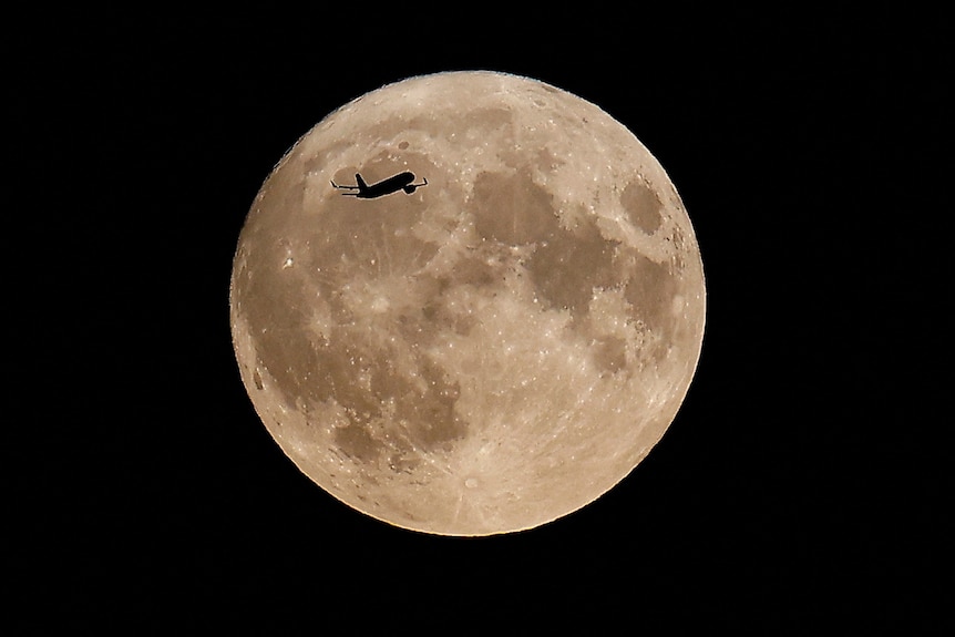 A plane flies over a giant moon