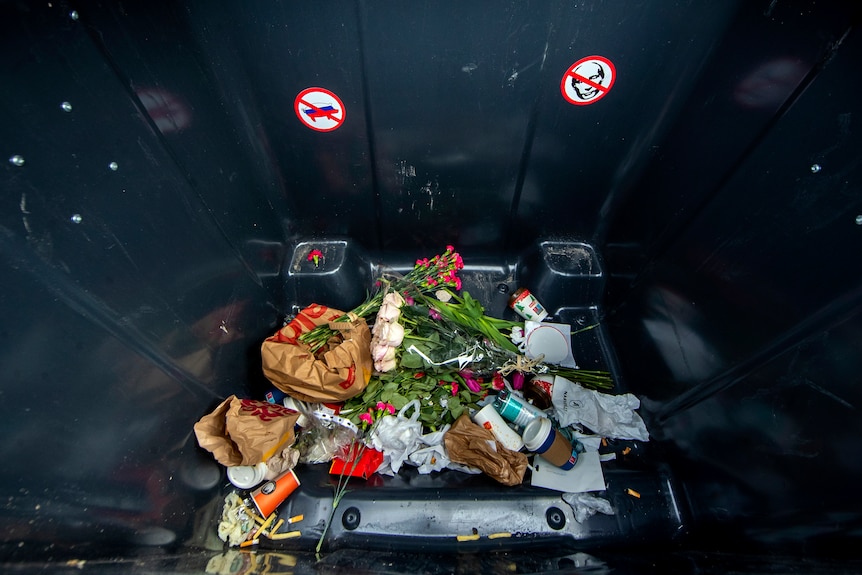 Flowers seen inside a garbage bin, along with an anti-Putin sticker placed inside.