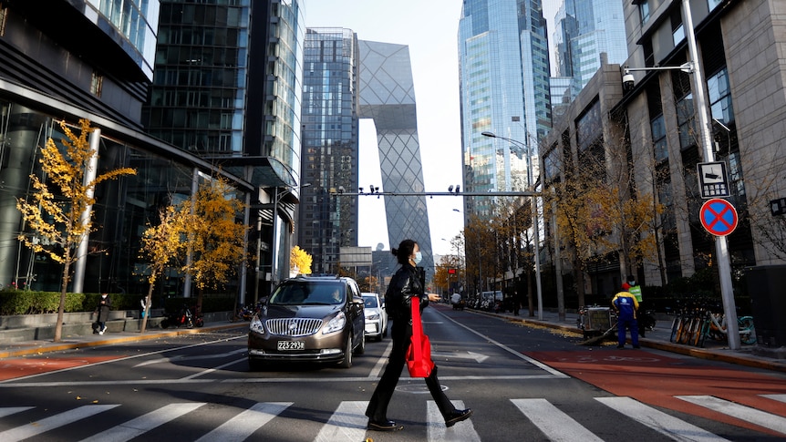 a woman in a face mask walks across a pedestrian crossing in a street in Beijing