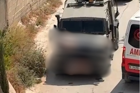 Blurred image of an army vehicle with a man tied to the front of it