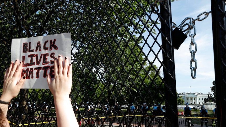 A person holds up a sign that reads "black lives matter" against a black fence erected around Lafayette Square.