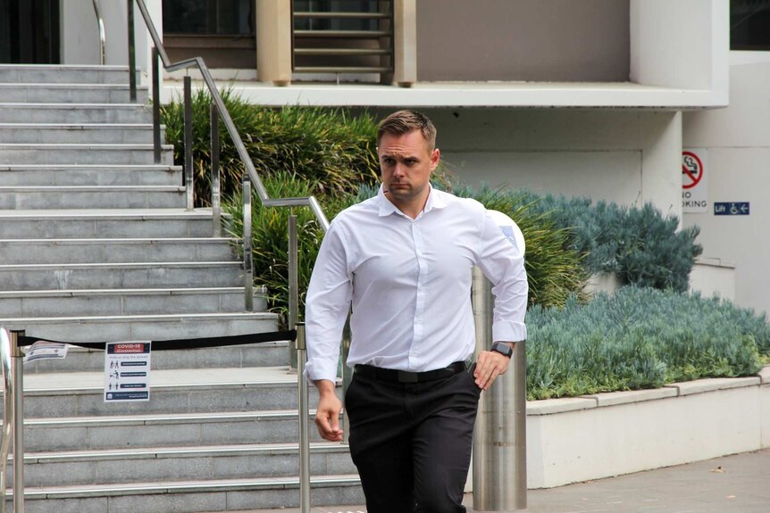 A man in a white business shirt and dress pants walking away from a court building.