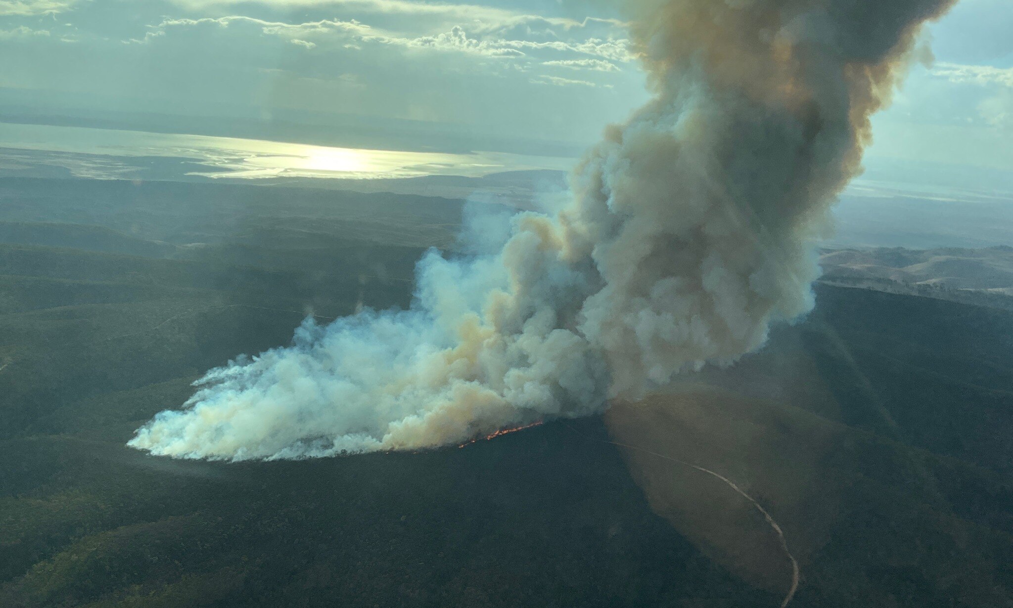 Large plumes of smoke rise from a fire burning across scrub land