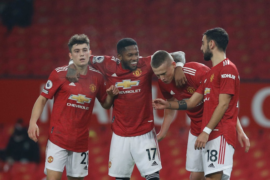 Quattro giocatori del Manchester United in maglietta rossa e pantaloncini bianchi sorridono e si abbracciano in fila