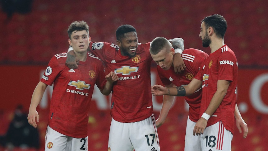 Four Manchester United players in red shirts and white shorts smile and hug in a line