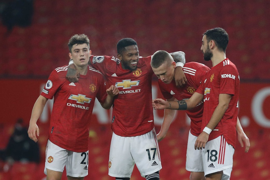 Four Manchester United players in red shirts and white shorts smile and hug in a line