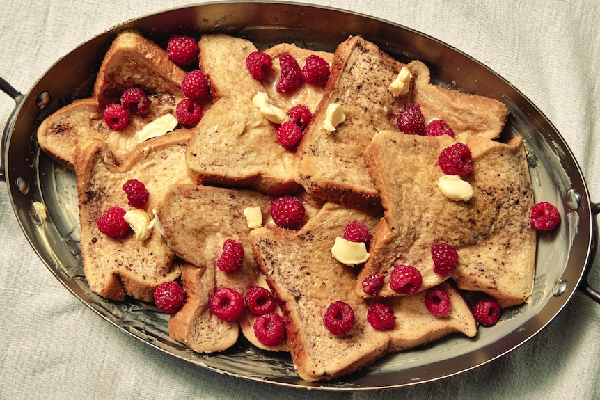 A baking tray of soaked bread, dotted with butter and raspberries before it's baked. An easy way to make French toast